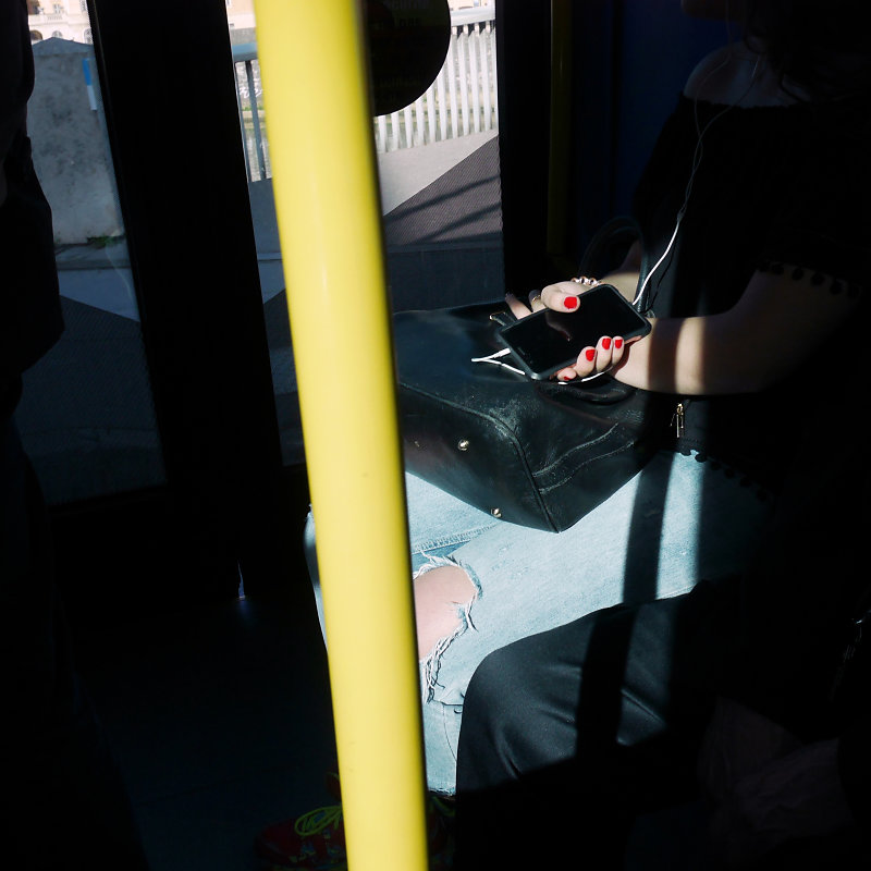 vernis rouge sur une main tenant son téléphone et barre jaune de maintien dans un bus